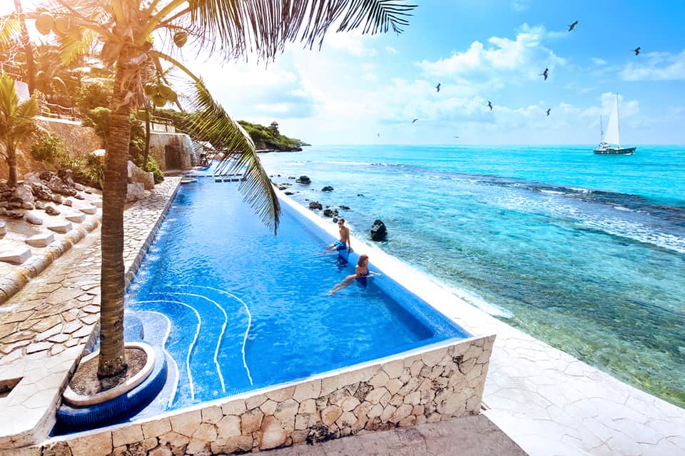 Infinity pool overlooking tropical ocean with palm trees and sailboat in distance