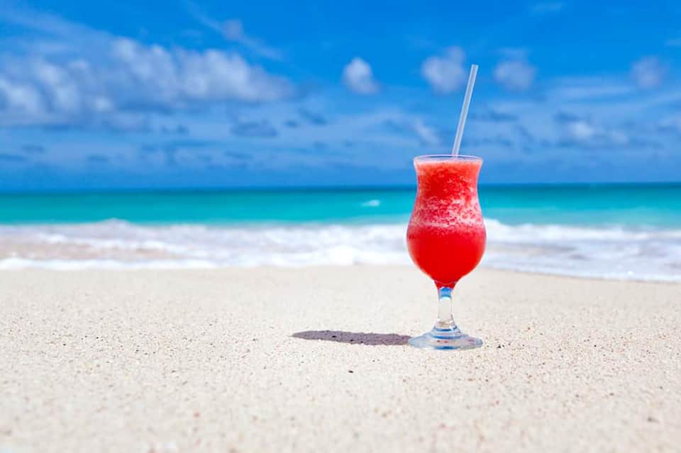 Red tropical cocktail on white sand beach with turquoise ocean and blue sky