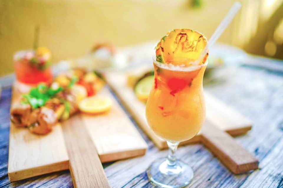 Tropical cocktail with pineapple garnish on wooden dining table with seafood appetizers