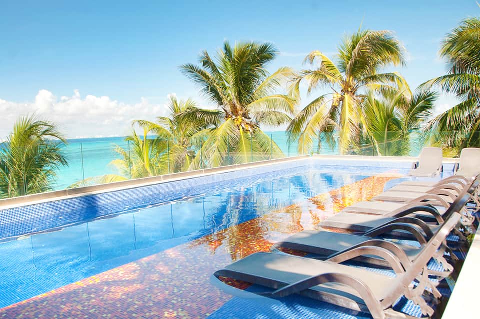 Oceanfront infinity pool with lounge chairs and palm trees overlooking turquoise water