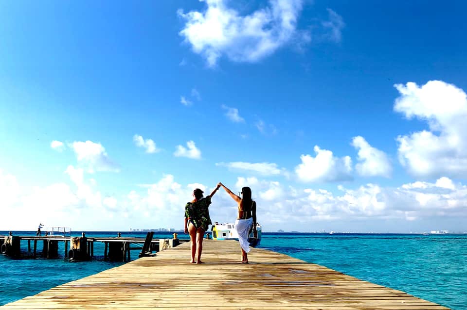 Two people celebrating on a wooden pier over turquoise ocean water under clear blue sky
