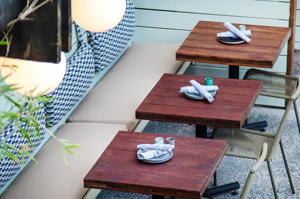 Outdoor dining tables with wood tops and patterned cushions set for service at beachfront resort
