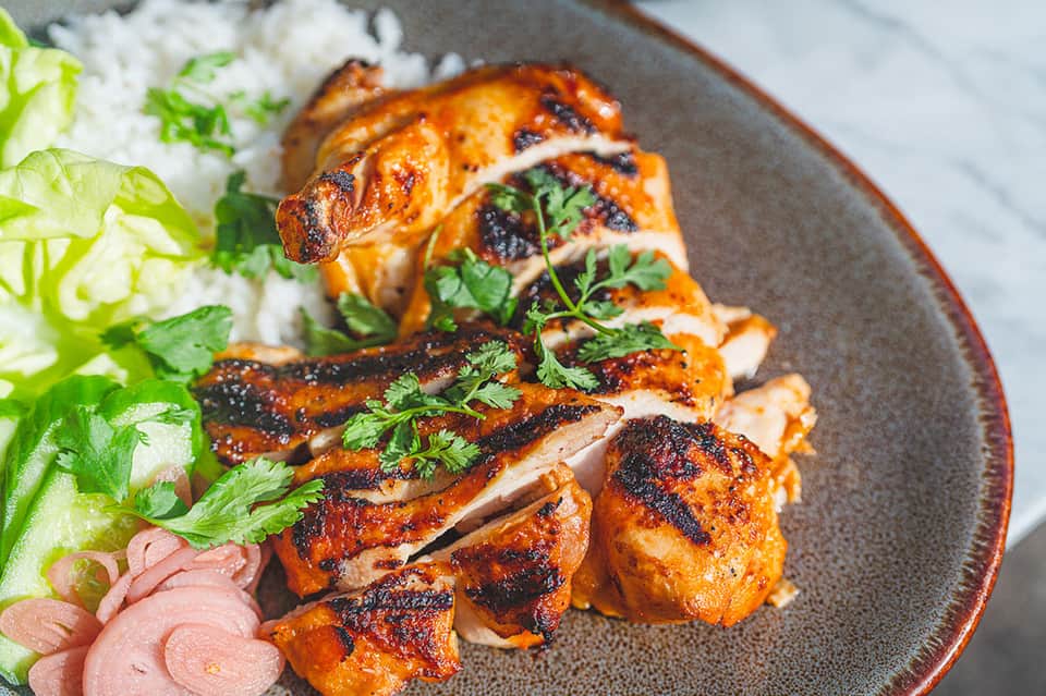 Roasted duck sliced and plated with jasmine rice, fresh herbs, and pink pickled vegetables