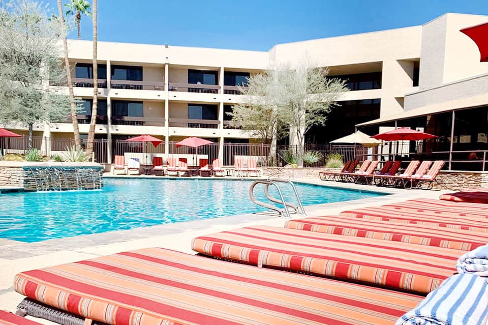 Resort pool area with striped lounge chairs, palm trees, and modern building