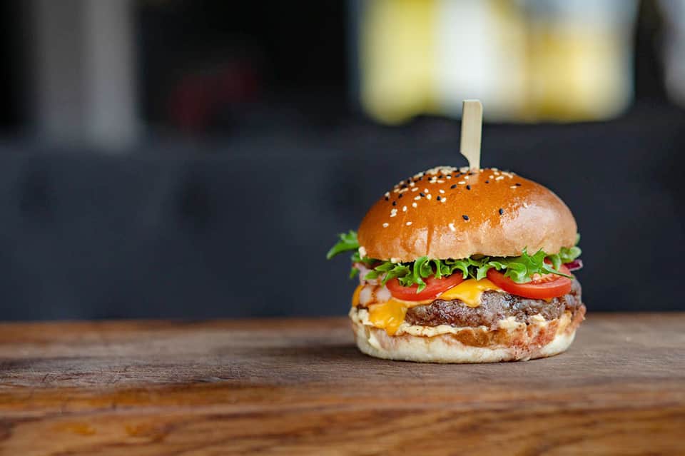 Gourmet cheeseburger with sesame seed bun, lettuce, and tomato on a wooden surface