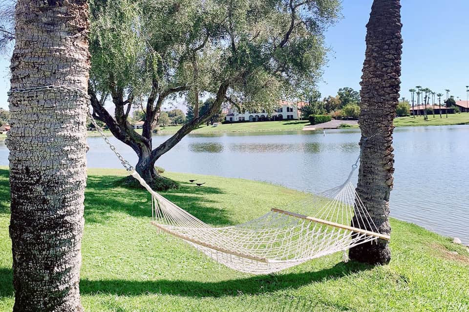 Hammock strung between palm trees overlooking a calm lake with white villa in background