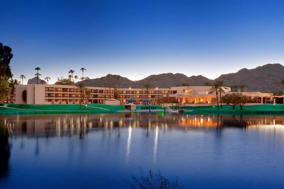 Modern resort building reflected in still water at dusk with mountains and palm trees