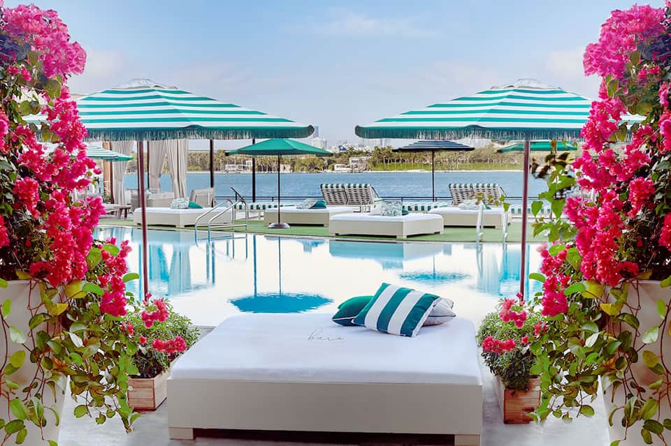 Waterfront daybed lounge surrounded by pink flowers with turquoise striped umbrellas and water view
