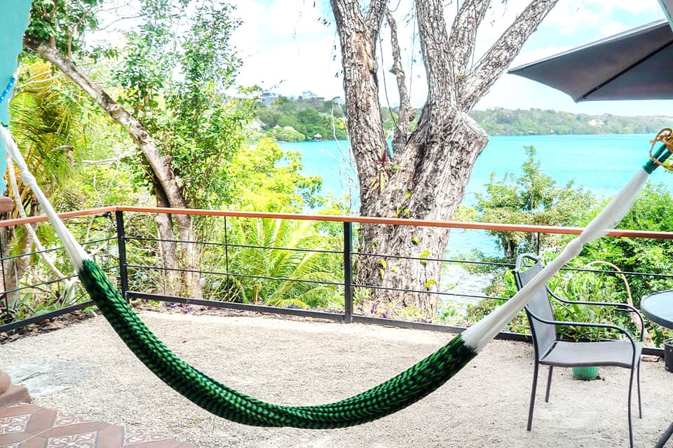 Green hammock overlooking turquoise water framed by large tree and tropical vegetation