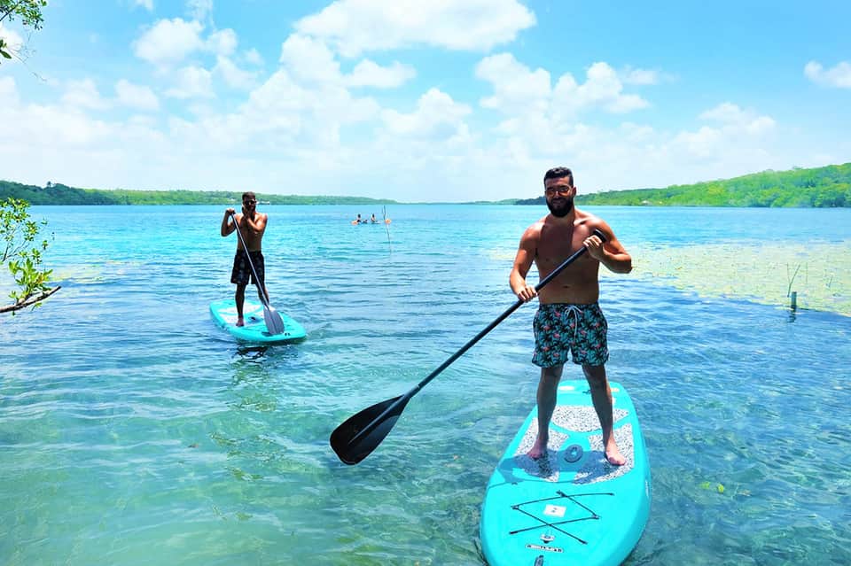Two people paddleboarding on crystal clear turquoise lagoon surrounded by tropical vegetation