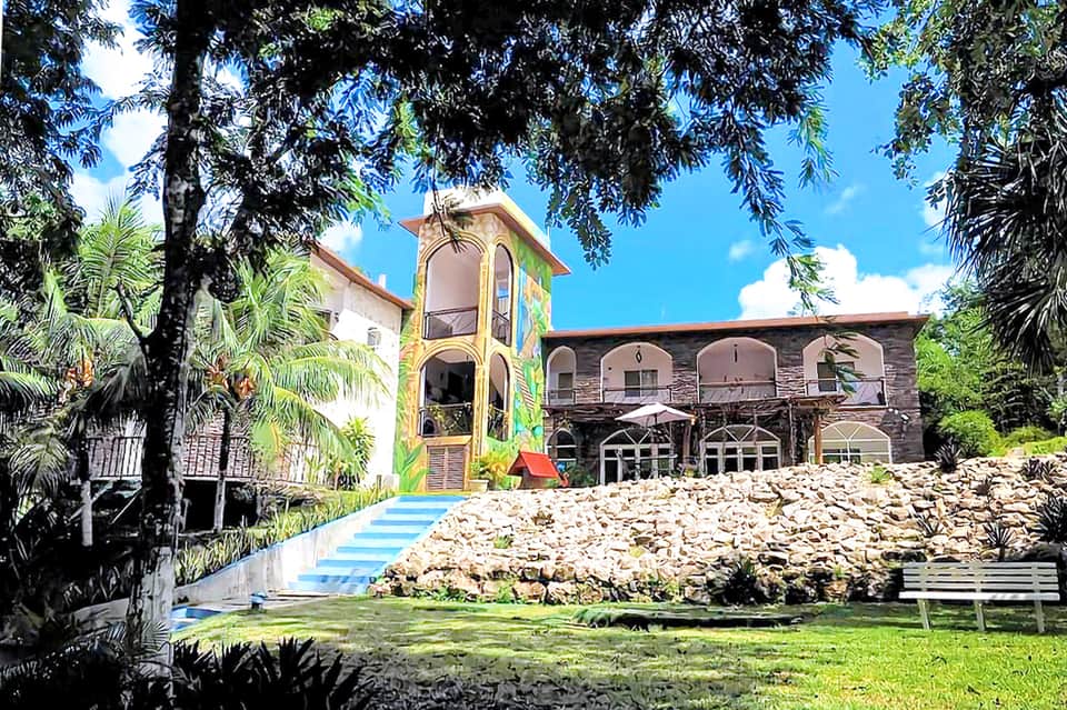 Colorful architectural building with yellow tower and stone structure nestled in green landscape