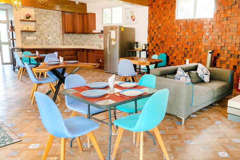 Open-concept common area with orange brick accent wall, turquoise chairs, dining table, and kitchen