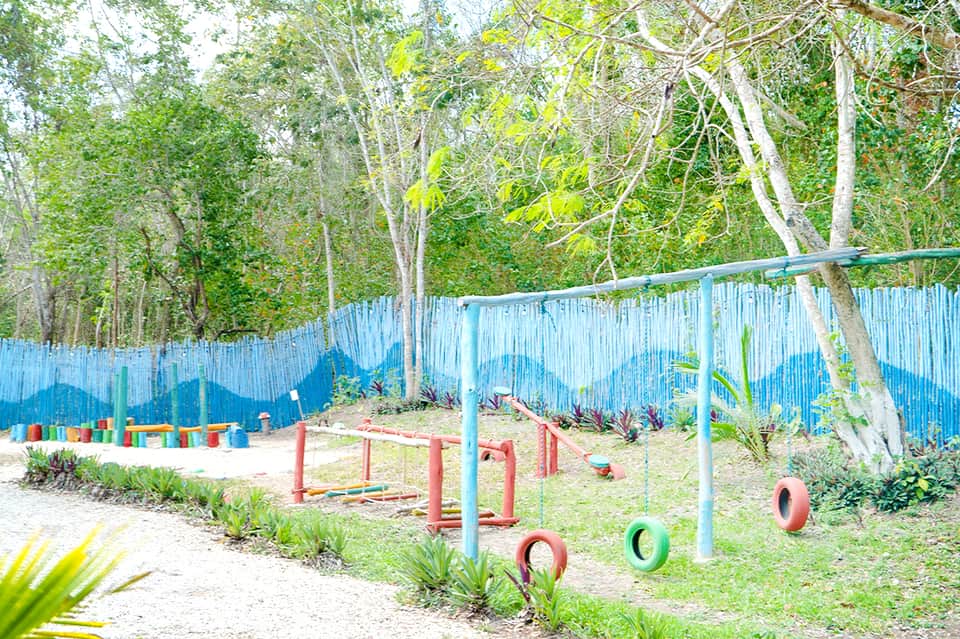 Colorful playground with tire obstacles and balance bars surrounded by blue fence and trees