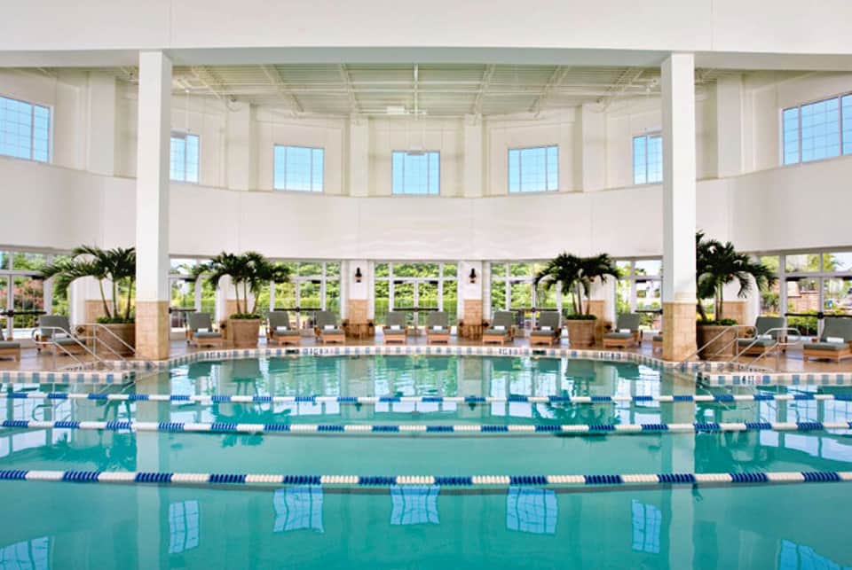 Indoor Olympic-sized swimming pool with lane markers, high ceilings, and natural light from large windows