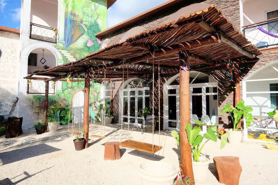 Rustic pergola with woven roof over sand patio with potted plants and modern building