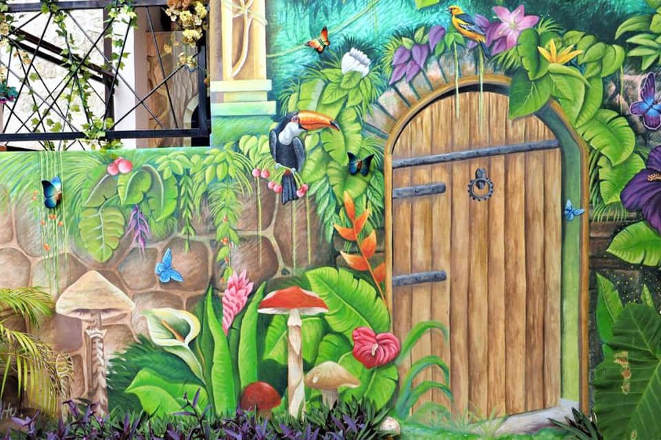 Vibrant mural of tropical jungle scene with wooden door, flowers, mushrooms, and colorful birds on stone wall