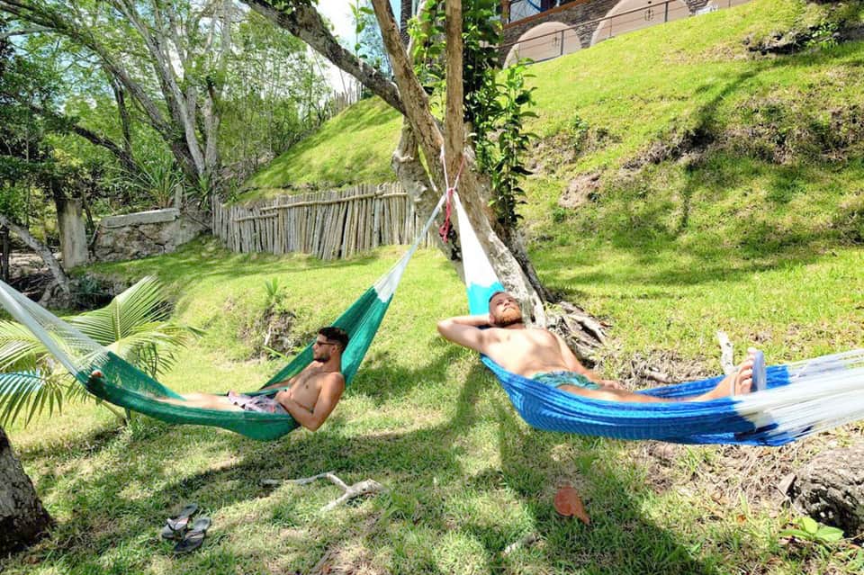 Two men relaxing in colorful hammocks in a lush green hillside garden setting