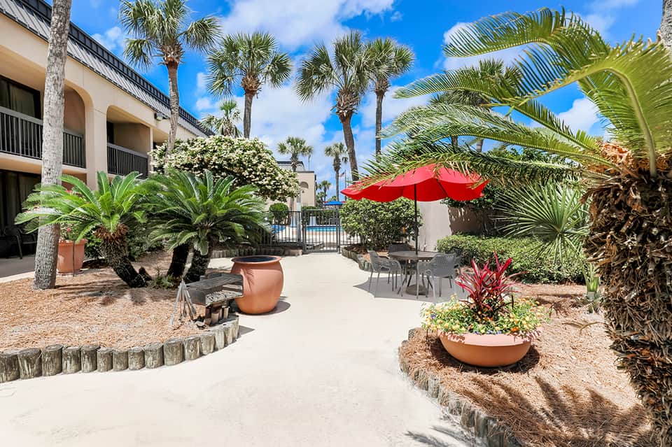 Tropical courtyard with red umbrella, palm trees, terracotta planters, and covered lounge areas
