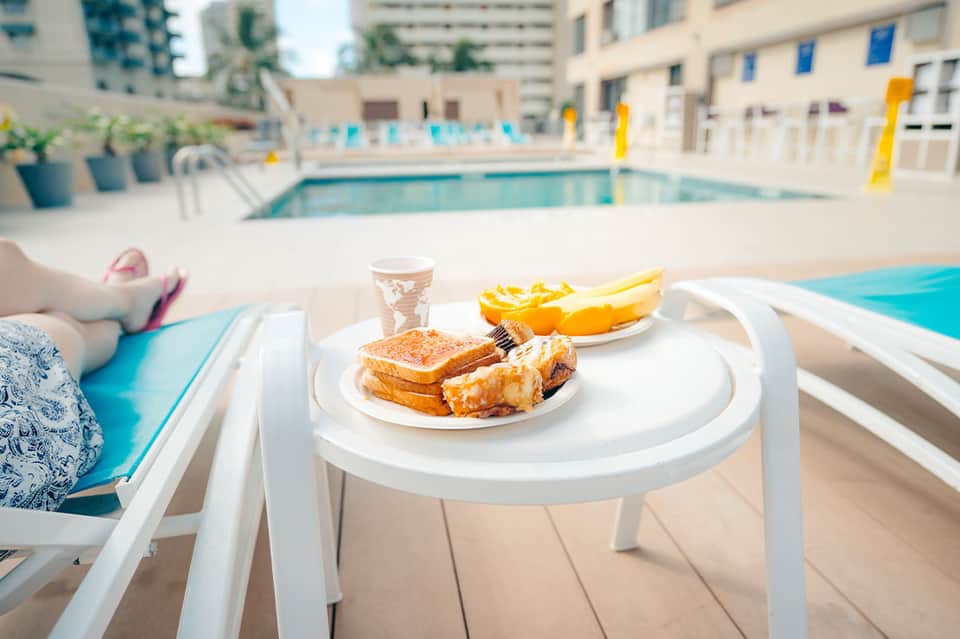 Poolside dining table with burger, fries, and beverage overlooking turquoise pool