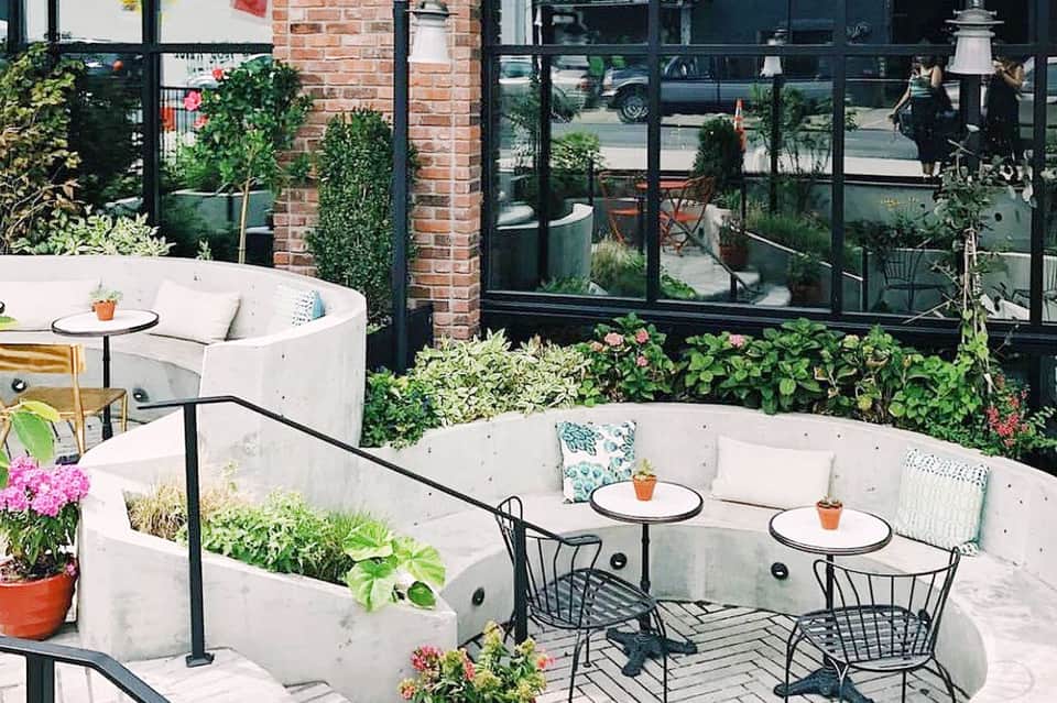 Rooftop outdoor lounge with white seating, green plants, brick accent wall, and city view