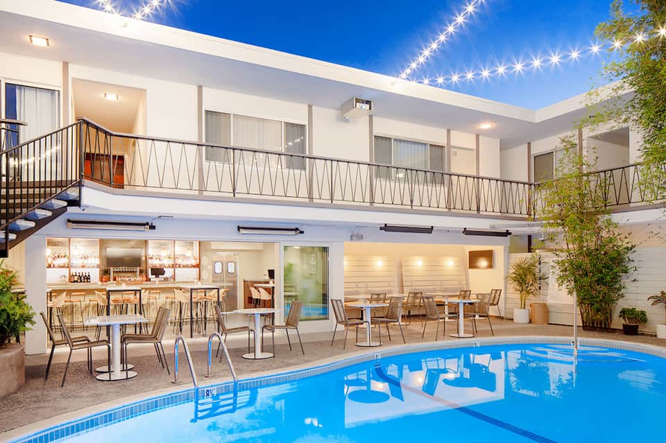 Contemporary pool area at night with illuminated terrace, bar, lounge chairs, and modern white building architecture