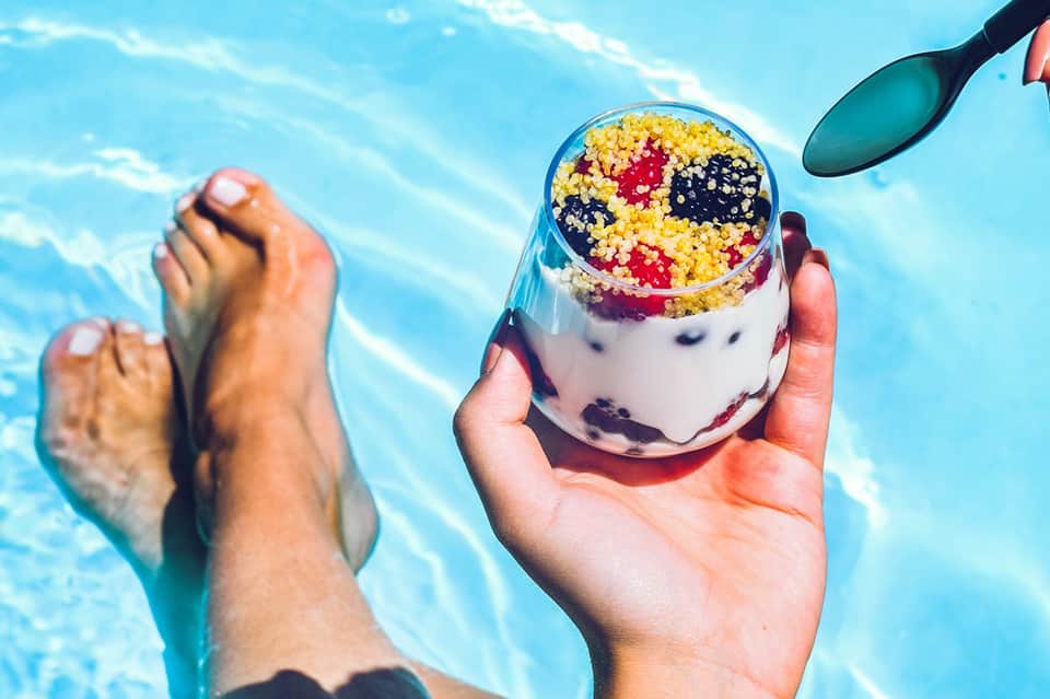 Close-up of colorful beverage with fruit cereal topping held above swimming pool water