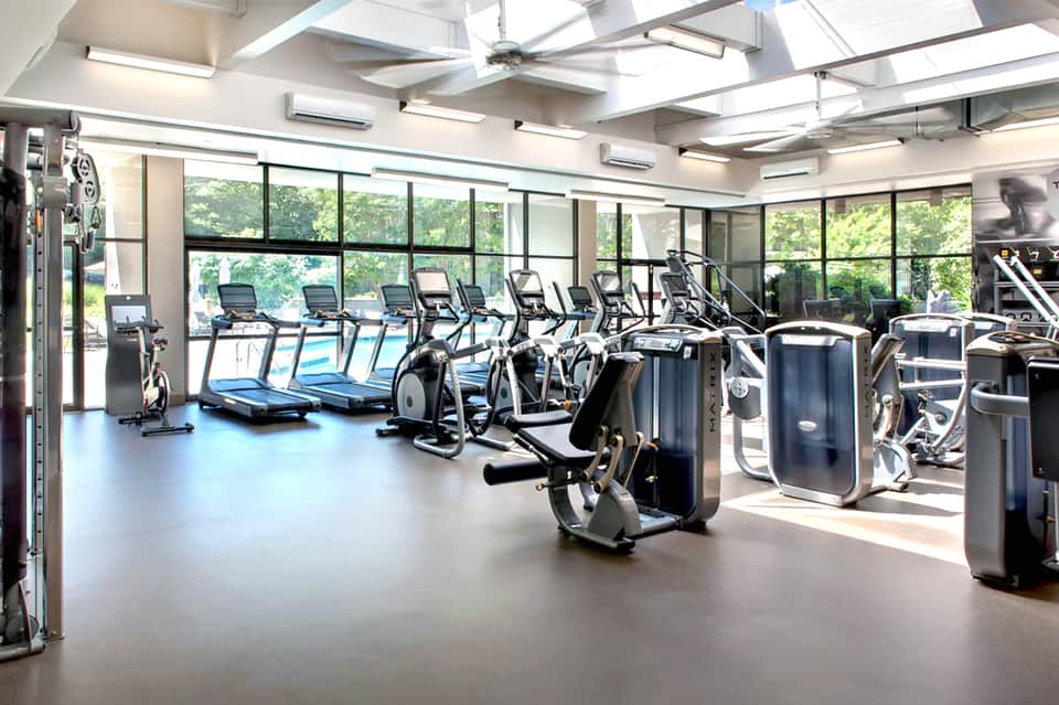 Bright fitness center with rows of treadmills, exercise bikes, and equipment with large windows