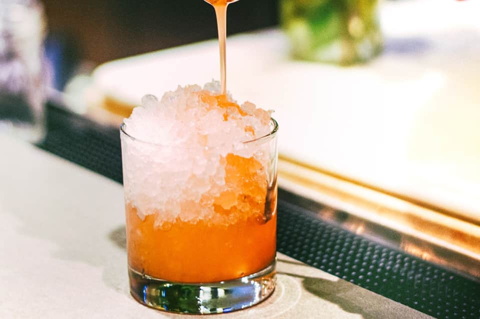 Craft cocktail with orange liquid and crushed ice being garnished at a resort bar
