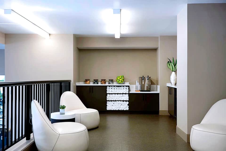 Modern spa reception area with minimalist design, white chairs, black accents, and neatly stacked towels