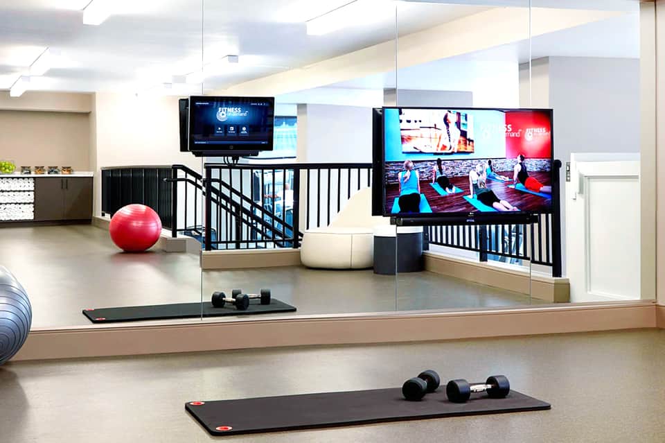 Modern fitness center with exercise equipment, large mirrors, screens, and dumbbells