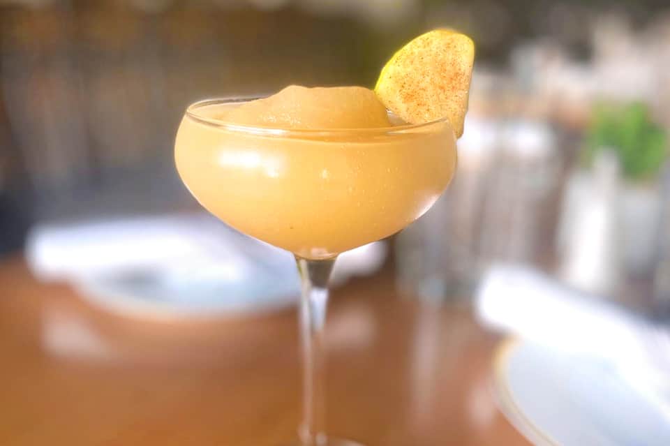 Golden cocktail drink with cinnamon chip garnish on blurred restaurant background