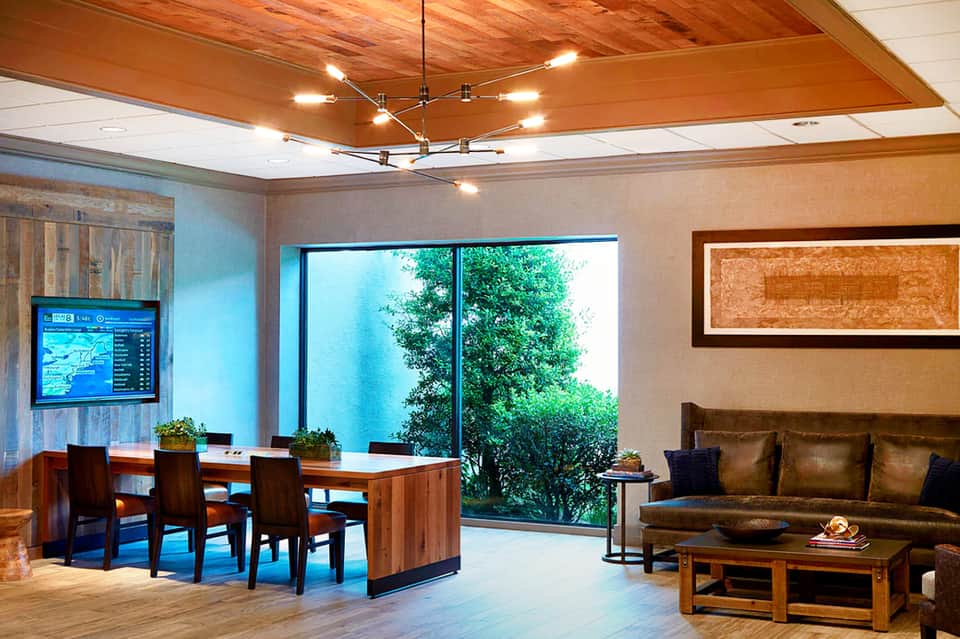 Modern lobby lounge with wooden ceiling, leather sofa, desk area, and large windows