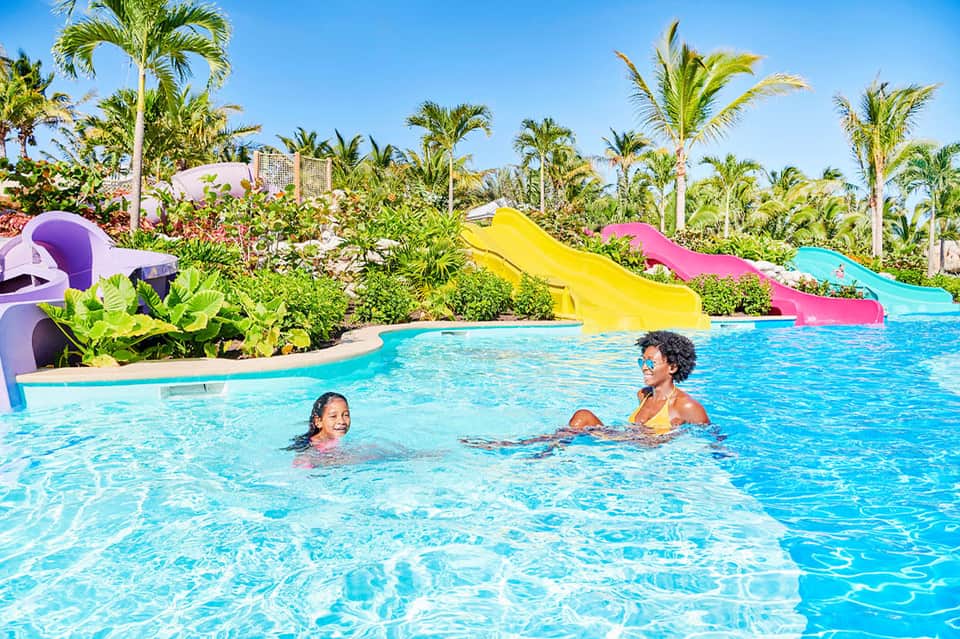 Family swimming in tropical resort pool with colorful water slides and palm trees
