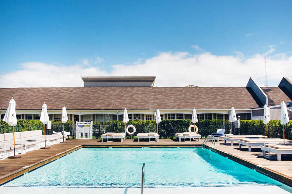 Resort outdoor swimming pool with turquoise water, white umbrellas, lounge chairs, and brick building backdrop