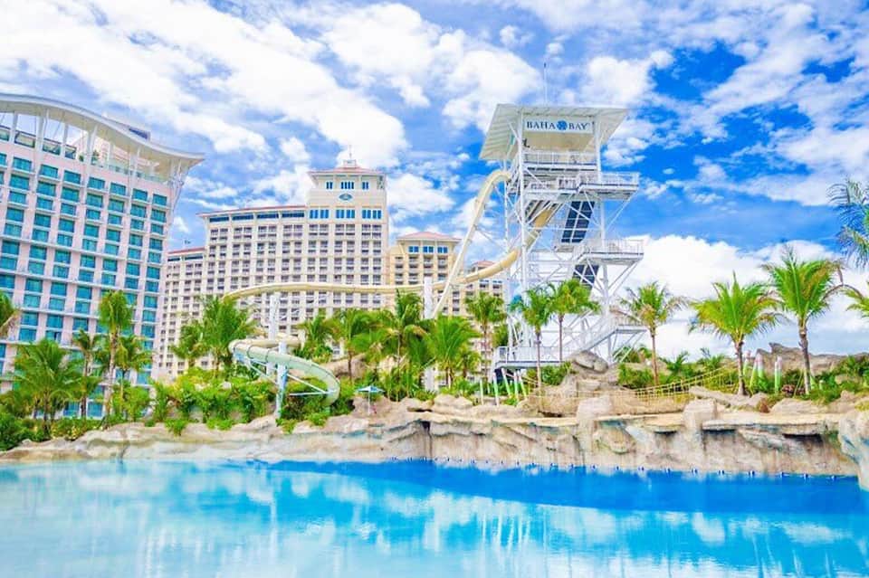Beachfront resort with sandy shore, palm trees, turquoise lagoon, and Bahia Bay water park with water slide