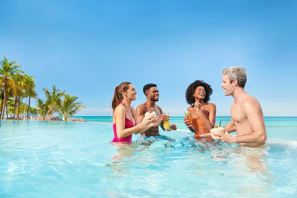 Four people in turquoise infinity pool with palm trees and ocean horizon