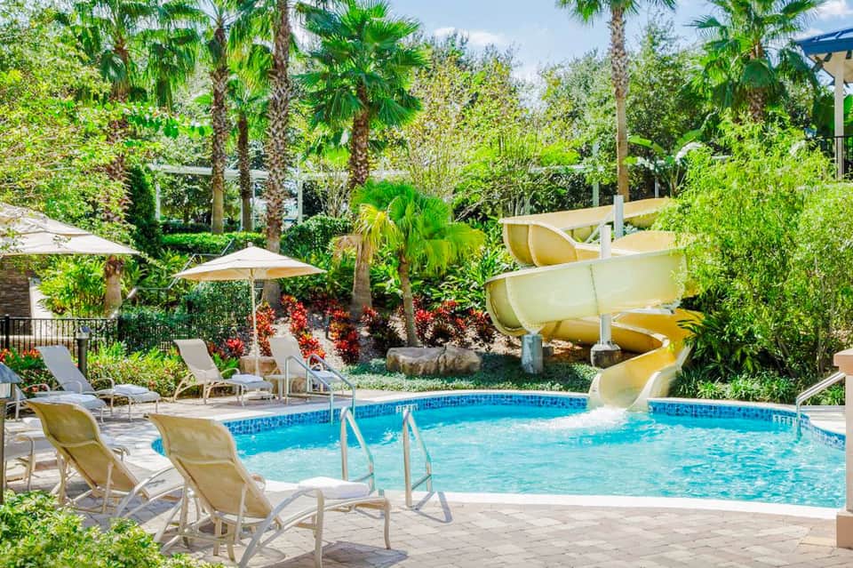Resort pool with water slides, tropical landscaping, lounge chairs, and umbrellas