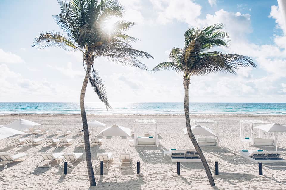 Beach with palm trees, white cabanas, and lounge chairs overlooking ocean