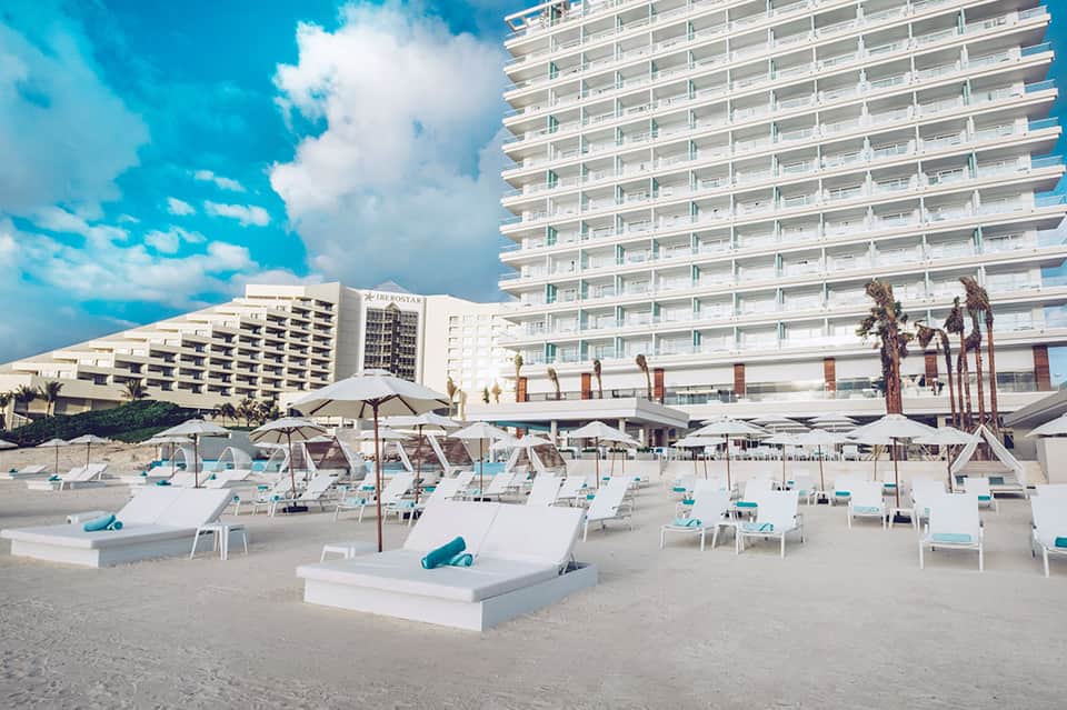 Modern beachfront resort with white lounge chairs, umbrellas, and tall hotel towers on sandy beach
