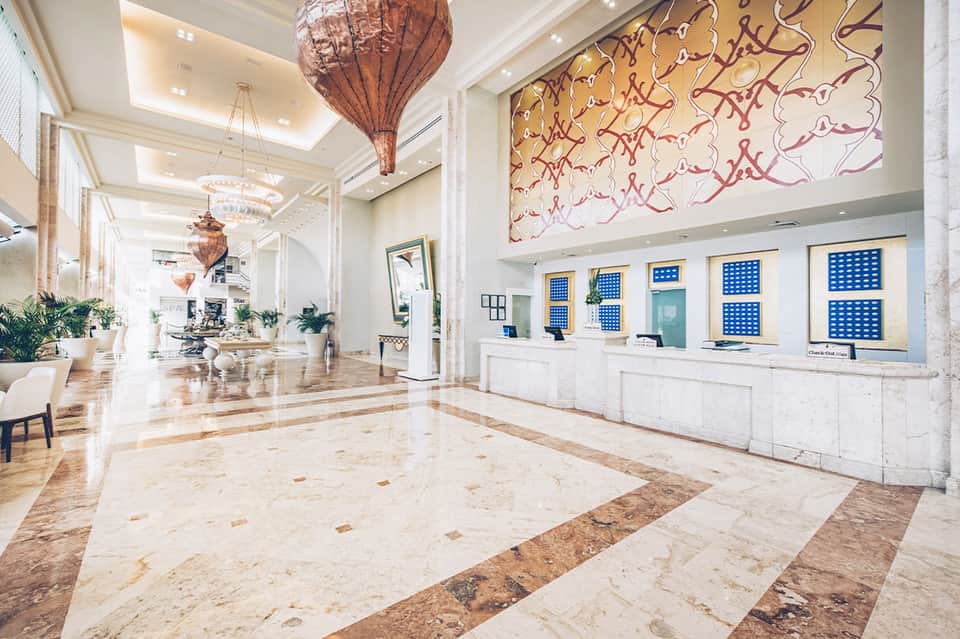Elegant hotel lobby with marble floors, artistic wall installation, and check-in desk