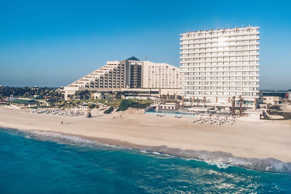 Beachfront resort hotel with white buildings, sandy beach, and turquoise ocean waves