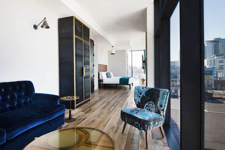 Luxury hotel suite with blue velvet sofa, bedroom view, and floor-to-ceiling windows overlooking city skyline
