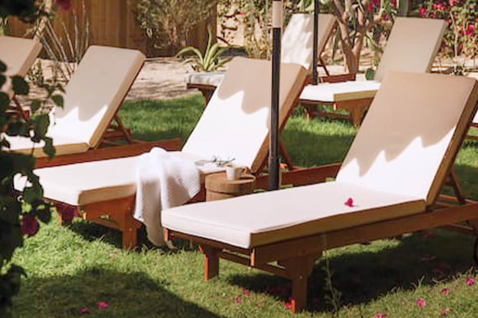 Wooden lounge chairs with white cushions arranged on manicured lawn surrounded by flowering plants