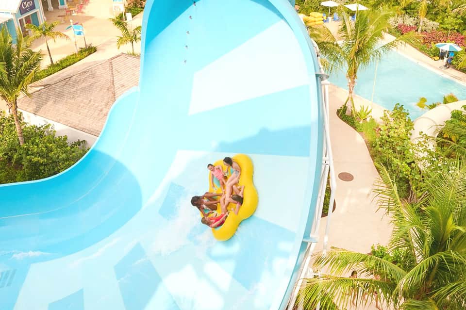Family on yellow water slide at resort pool surrounded by palm trees