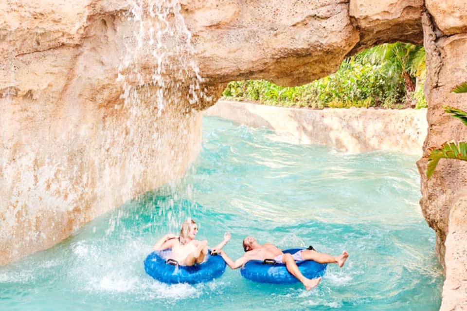 Two men floating on blue tubes in crystal turquoise water between rocky limestone cliffs
