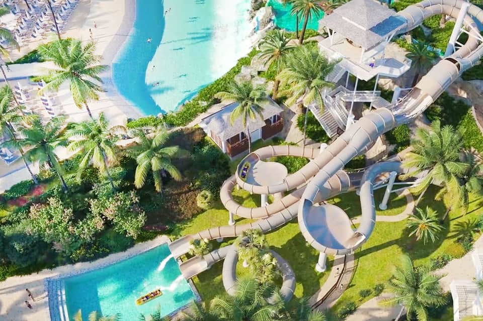 Aerial view of resort with turquoise pools, water slides, palm trees, and manicured grounds