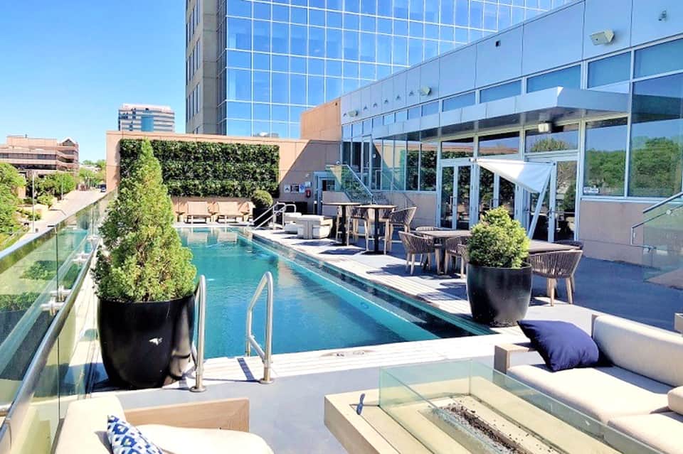 Rooftop pool area with turquoise lap pool, lounge chairs, and city skyline views