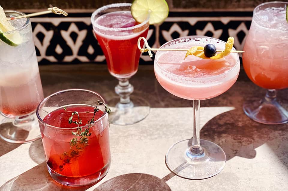 Colorful cocktails with fruit garnishes served on outdoor patio with decorative patterned backdrop
