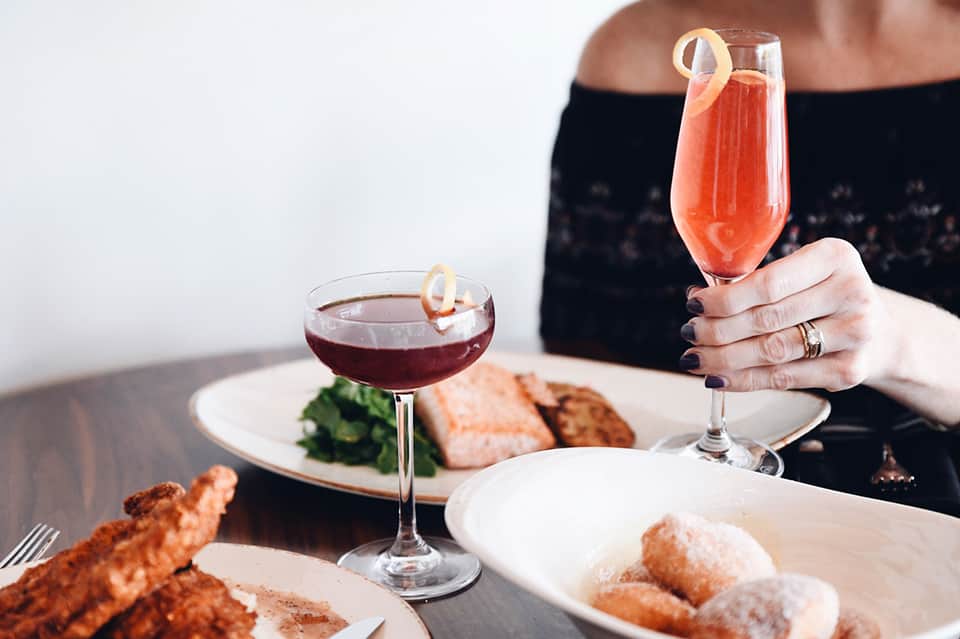 Woman holding cocktails at dining table with plated food and elegant glassware
