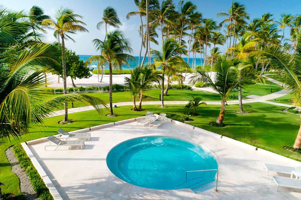 Beachfront resort with pool, palm trees, lounge chairs, and ocean beyond